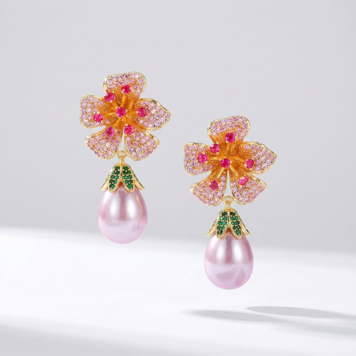 Hamida pink flower drop earrings hanging from a branch, showcasing the intricate green crystal leaf cap and pink faux pearl details. 