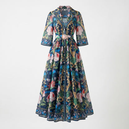 The Judith Maxi Dress in cream and navy featuring a floral baroque print, notched collar, button-down front, and a matching gold buckle belt on a flat lay display.