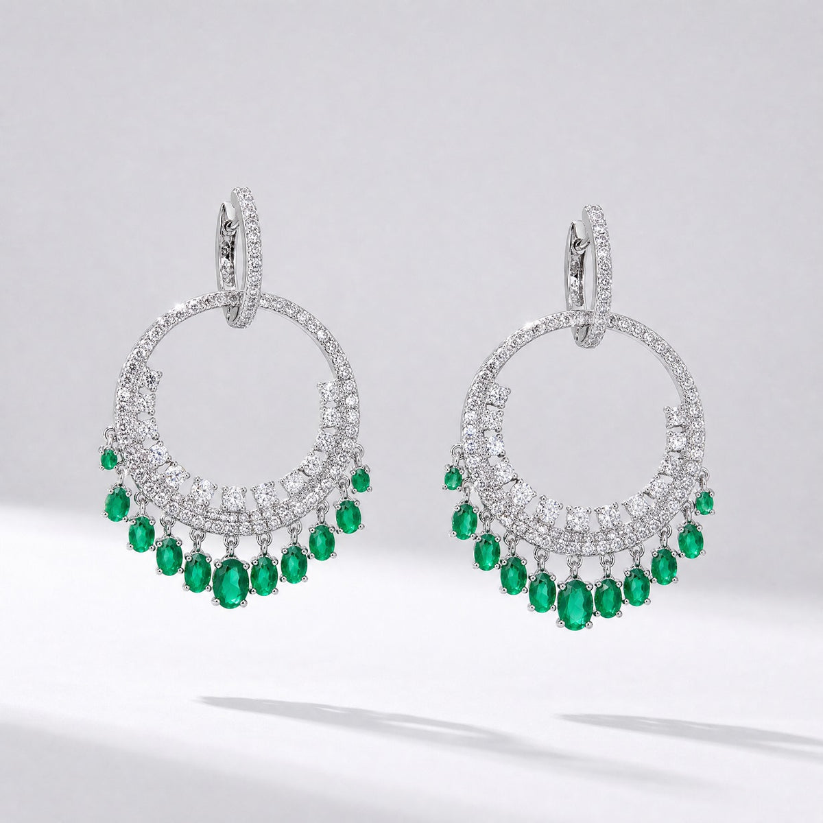 Pair of silver Laura tassel earrings featuring a circular cubic zirconia hoop with green emerald-colored water drop charms hanging from the bottom.