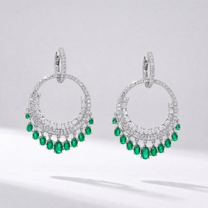 Pair of silver Laura tassel earrings featuring a circular cubic zirconia hoop with green emerald-colored water drop charms hanging from the bottom.