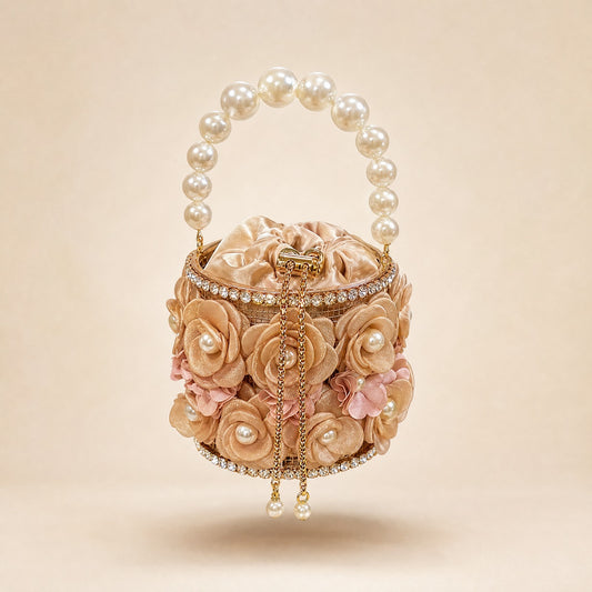 Nandini small floral bucket clutch bag in champagne with a large pearl handle and rhinestone detailing  small floral evening clutch bag by its white pearl handle, showcasing the 3D rose fabric design and crystal trim.