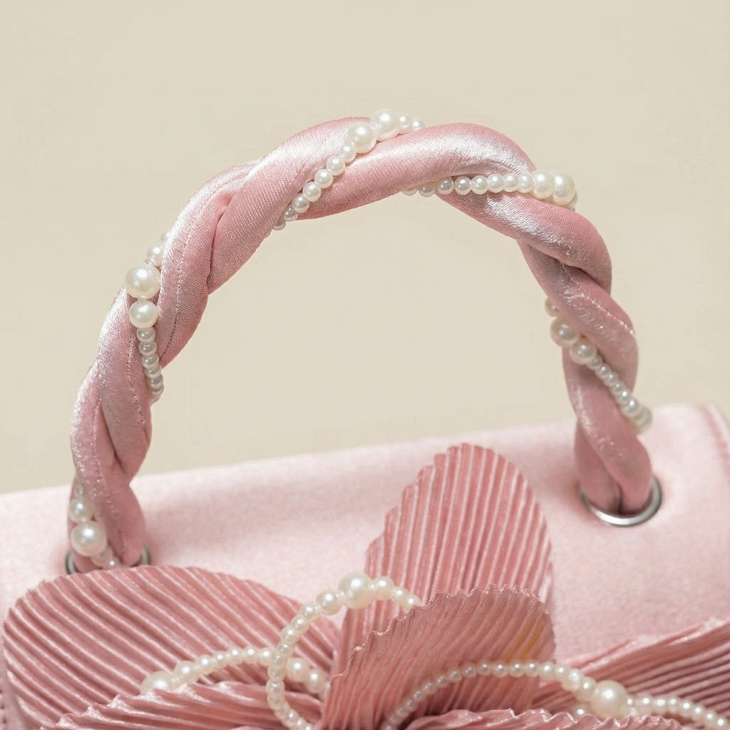 Close-up of pink clutch showing braided handles and cream pearl details