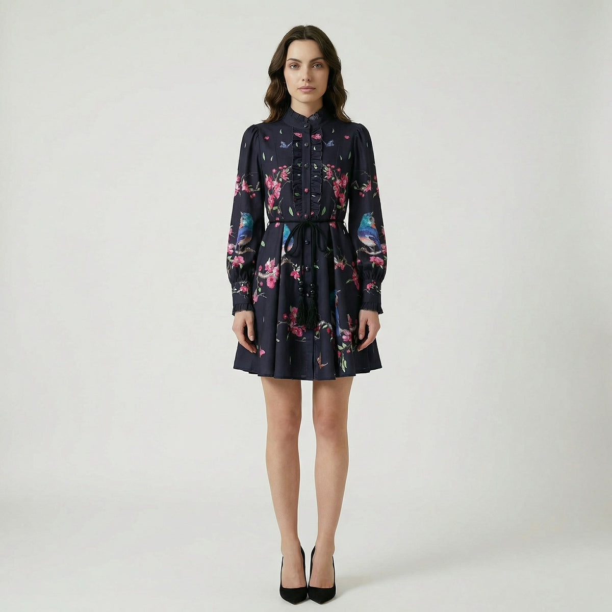 A ruffled mini dress named Suzanne featuring a print of blue birds, pink blossoms, and butterflies, shown in black and cream color options.