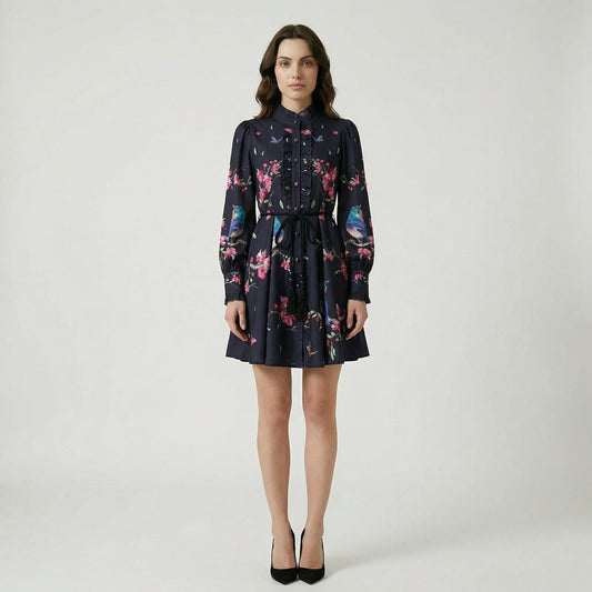 A ruffled mini dress named Suzanne featuring a print of blue birds, pink blossoms, and butterflies, shown in black and cream color options.